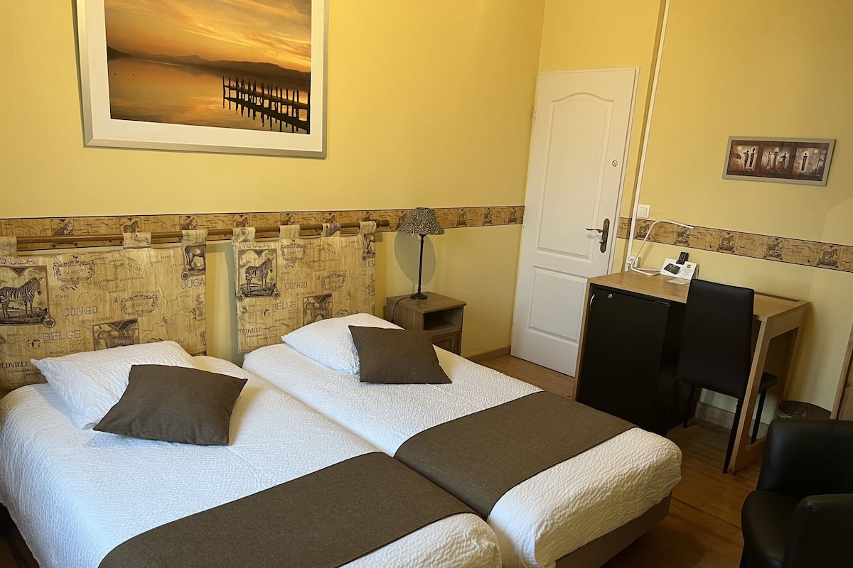 Habitación de hotel con dos camas, un escritorio, una silla, una puerta y un cabecero decorado con motivos de mapa.