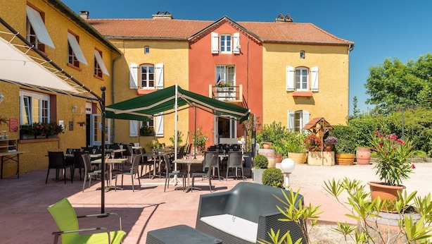 Un patio al aire libre con mesas y sillas, rodeado de edificios con fachadas rojas y amarillas.