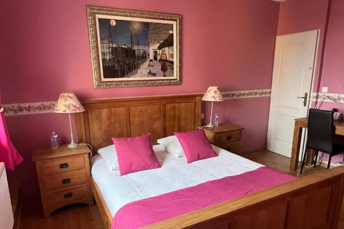 Un dormitorio con una cama de madera, dos mesitas de noche, un buró, un escritorio y una silla.