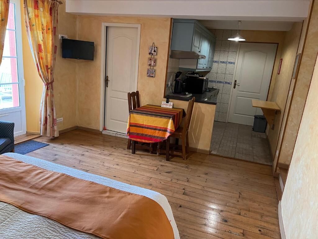 Una habitación compacta con cama, una mesa de comedor con sillas, una kitchenette y una puerta que da a otra habitación.