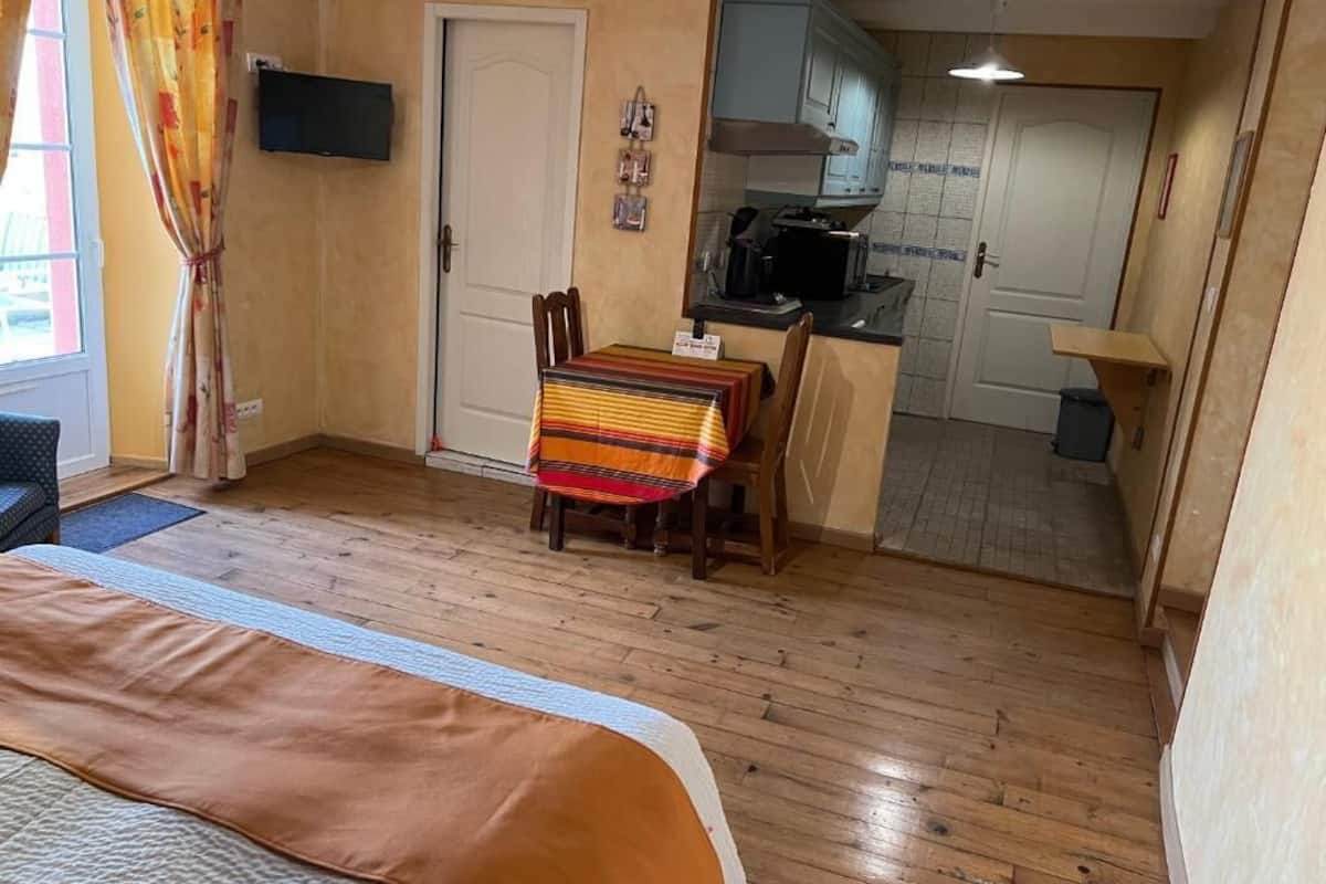 Una habitación compacta con cama, una mesa de comedor con sillas, una kitchenette y una puerta que da a otra habitación.