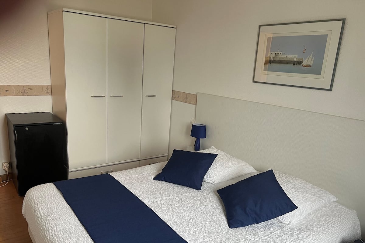 Habitación de hotel con cama, armario, escritorio y un cuadro en la pared.