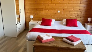 Un dormitorio con techo de madera, cama con ropa de cama roja y blanca, dos mesitas de noche con lámparas y un aparador de madera.