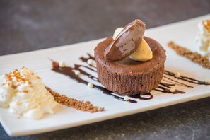 Un dessert composé d’un gâteau au chocolat, d’une boule de glace et d’une portion de crème fouettée, le tout présenté sur une assiette blanche.