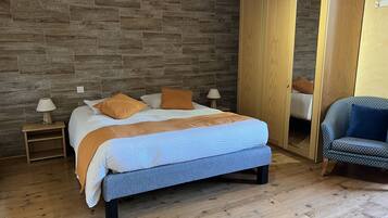 Une chambre à coucher comprenant un lit, deux tables de chevet, une armoire en bois et un fauteuil à motifs.