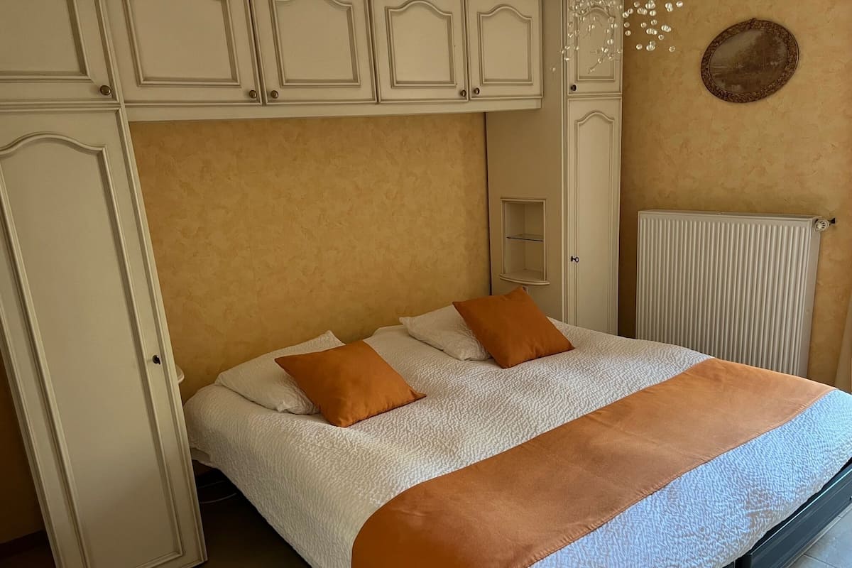 Un dormitorio con cama, paredes blancas, radiador y armario.