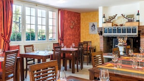 Un restaurante con mesas y sillas de madera, copas de vino y un cartel con el menú sobre la chimenea.