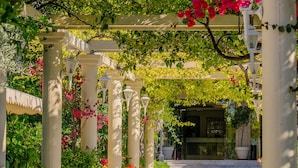 Une allée couverte, ornée de colonnes blanches et de fleurs roses.