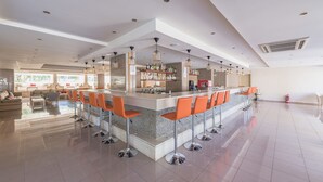 Un grand espace bar doté de nombreux tabourets, d’un comptoir bien garni et d’un vaste coin salon avec un canapé et des fauteuils.