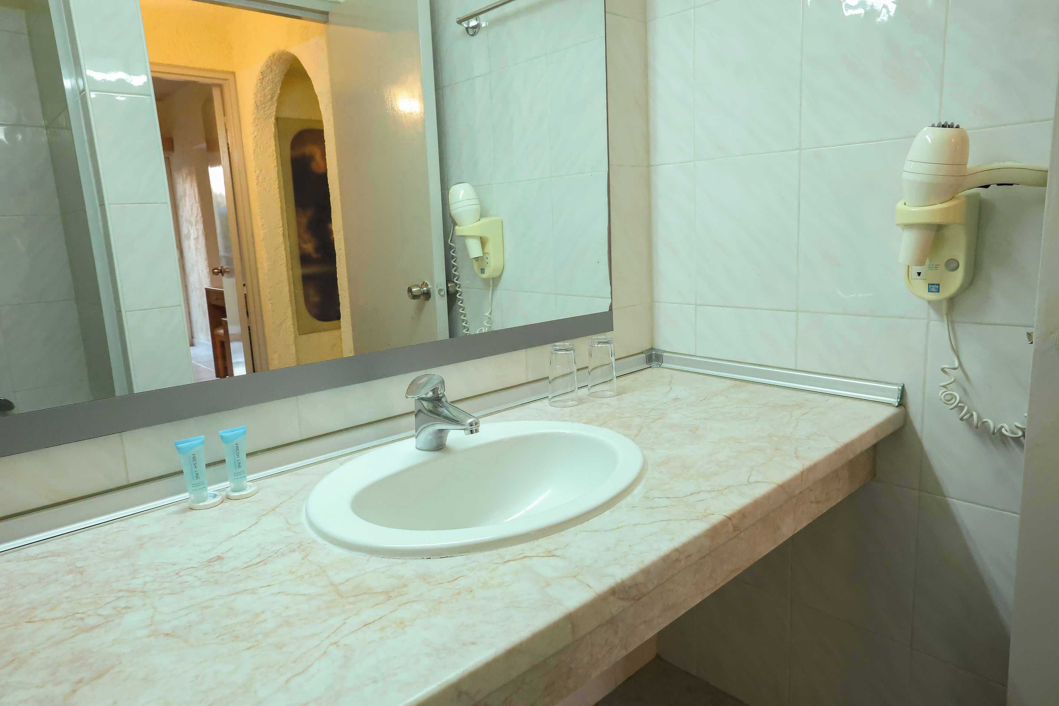 A bathroom with a white sink, a mirror, and a hairdryer mounted on the wall.