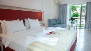 A hotel room with a large bed, a bedside table with a vase of flowers, a small table with a chair, and a view of the outdoors through a sliding door.