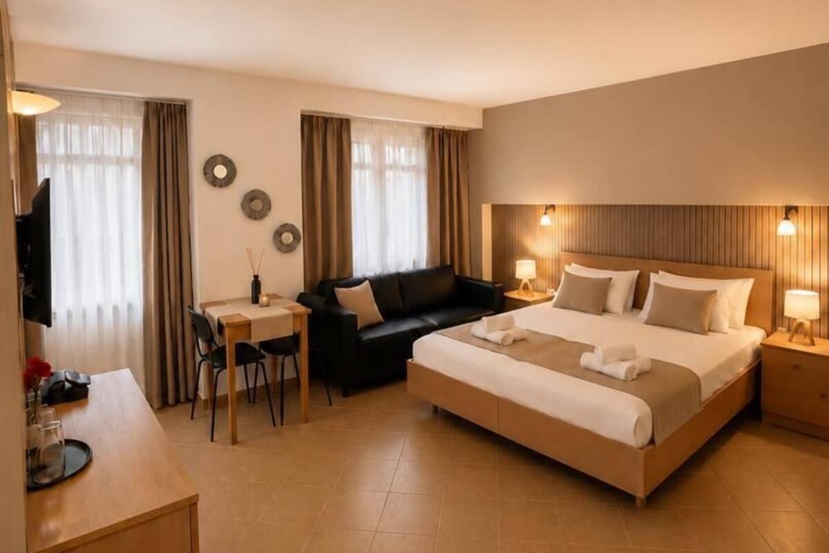 A hotel room with a bed, a sofa, a desk, and a TV.
