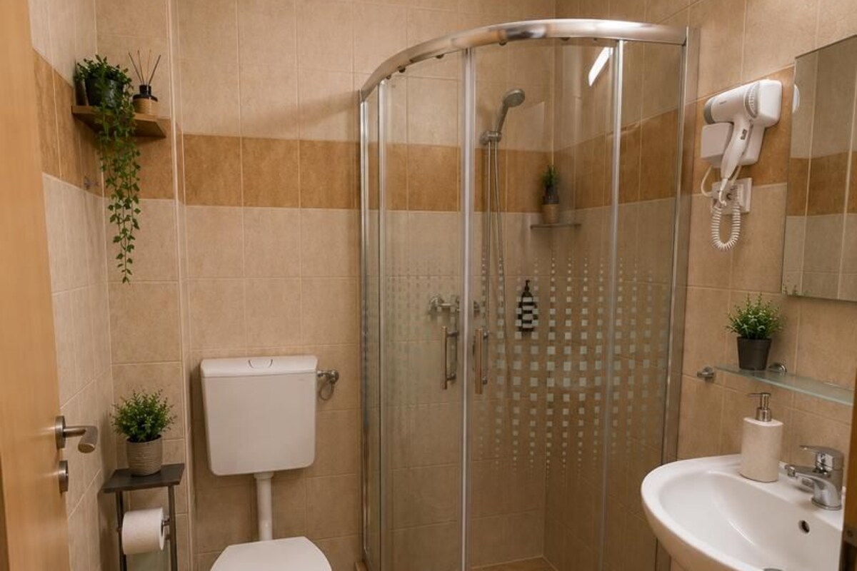 A bathroom with a glass-enclosed shower, a toilet, a sink, and a trash can.