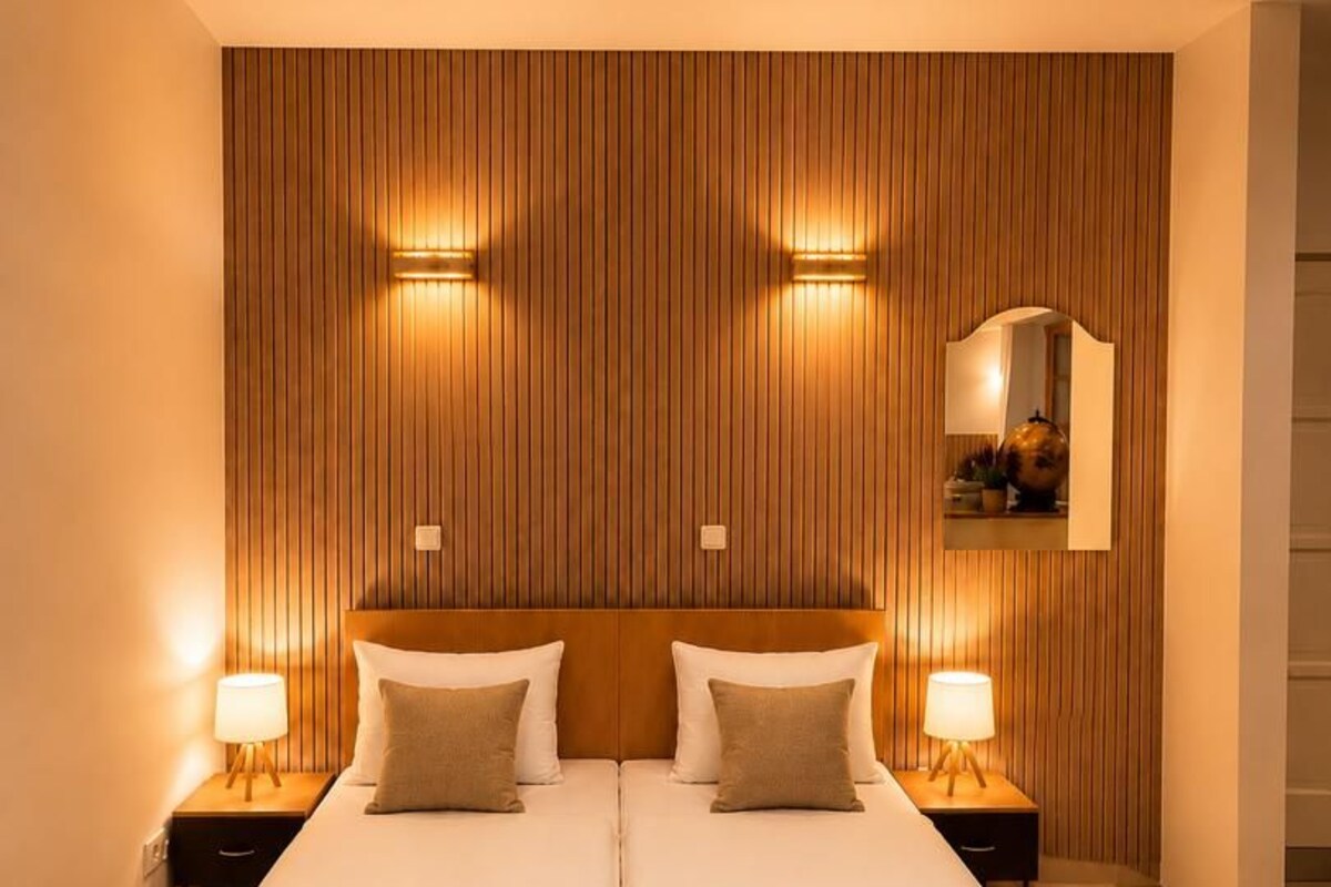 A double bed with two nightstands, a wooden panel wall, and a mirror above the bed.