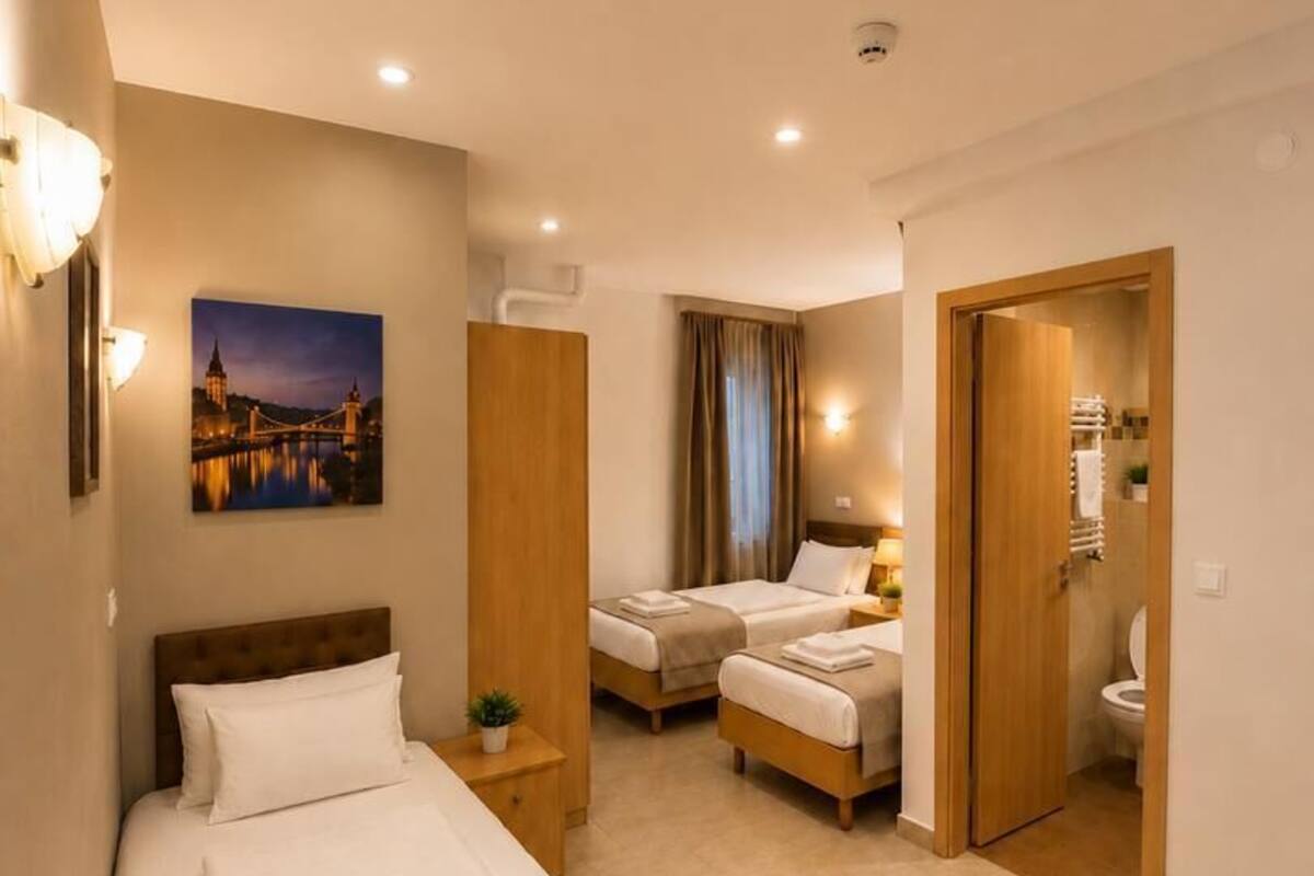 A hotel room with a bed, two bedside tables, a nightstand, a bathroom, and a door leading to another room.