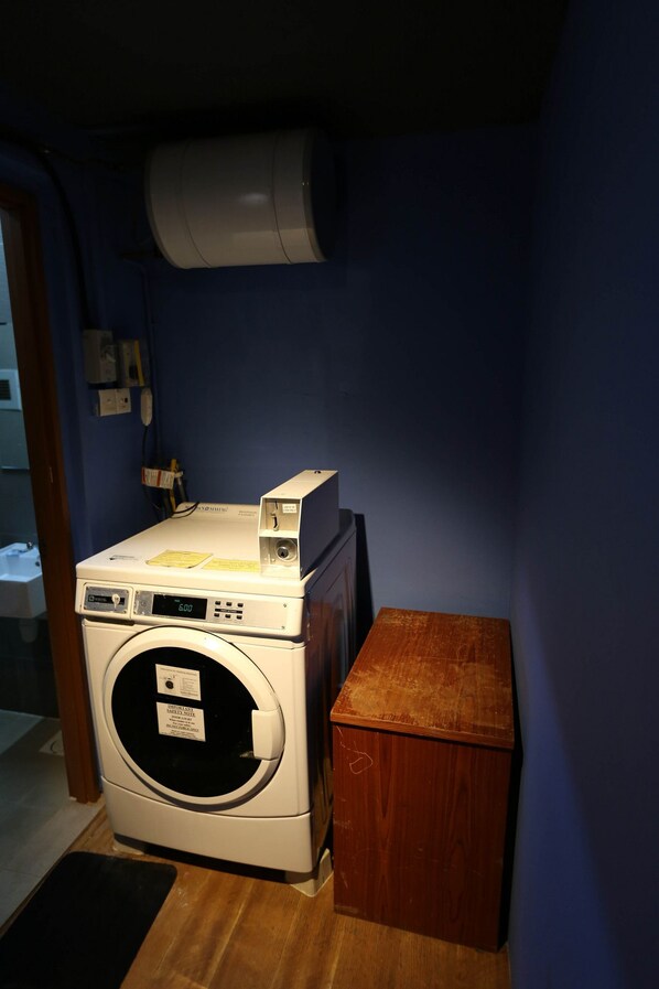 A compact laundry room with a front-loading washing machine, a drying machine, and a small wooden cabinet. - Fernloft City Little India (Singapore)