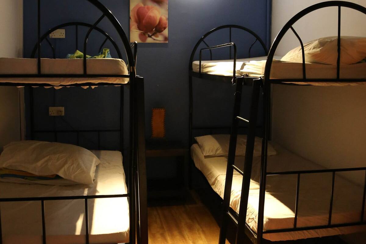 Une chambre de dortoir avec des lits superposés, un tapis rouge et un luminaire fixé au mur.