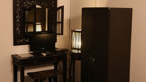 Une petite pièce comprenant un bureau, une chaise, un lit, un miroir et une horloge fixée au mur.