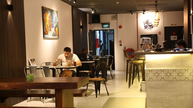 L’intérieur d’un restaurant, avec des tables et des chaises, un panneau indiquant la sortie et un comptoir avec une machine à café.