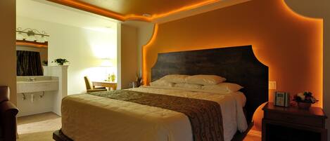A hotel room with a large bed, a bedside table, a nightstand, a mirror, and a bathroom with a sink and towel rack.