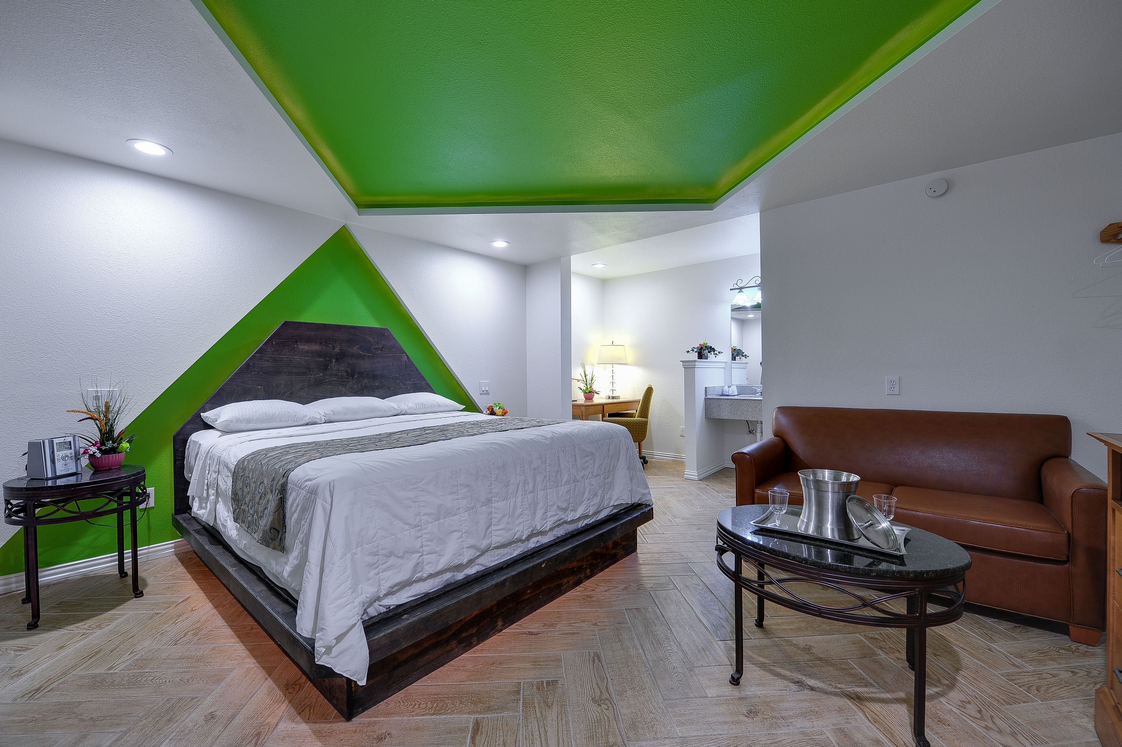 Une chambre à coucher moderne avec un lit, un canapé en cuir marron, une petite table et un mur d’accent vert.