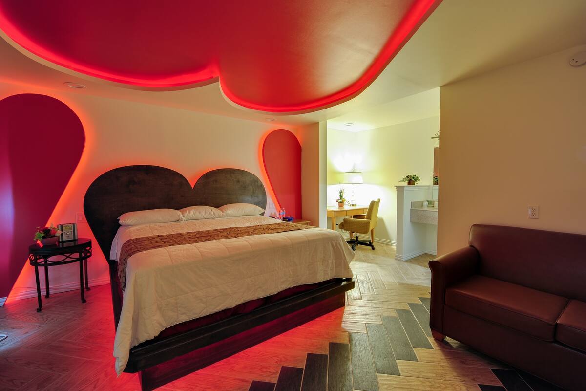 Un dormitorio moderno con una cama grande, una pared de acento roja y suelo de madera.