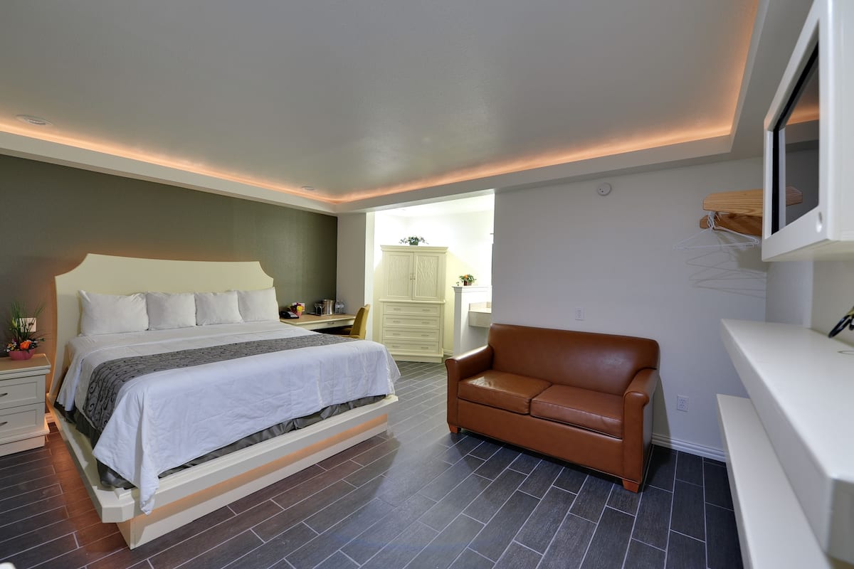 Un dormitorio moderno con una cama grande, un sofá de cuero marrón, un aparador blanco y un televisor montado en la pared.