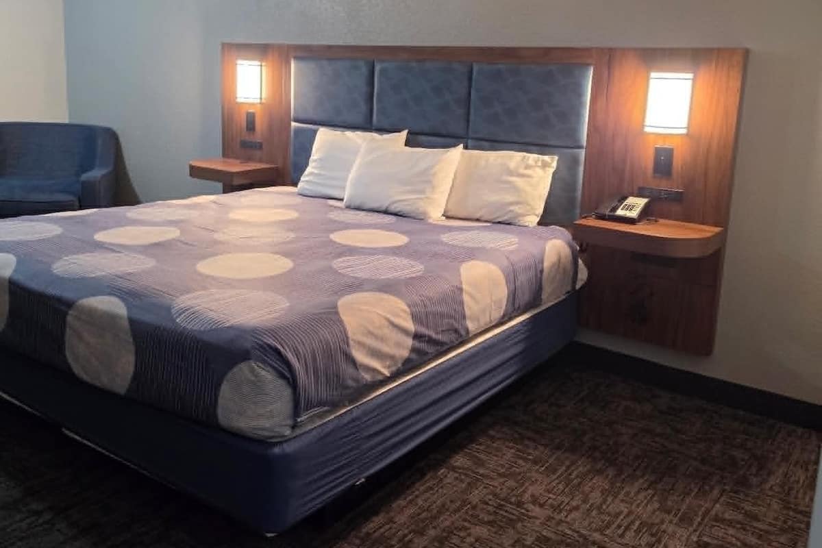 A hotel room with a bed, two bedside tables, a chair, and a wooden headboard.