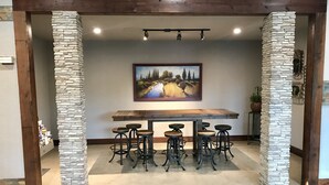 Un comedor con una mesa de madera y seis taburetes, enmarcado por pilares de piedra, bajo un techo con iluminación empotrada.