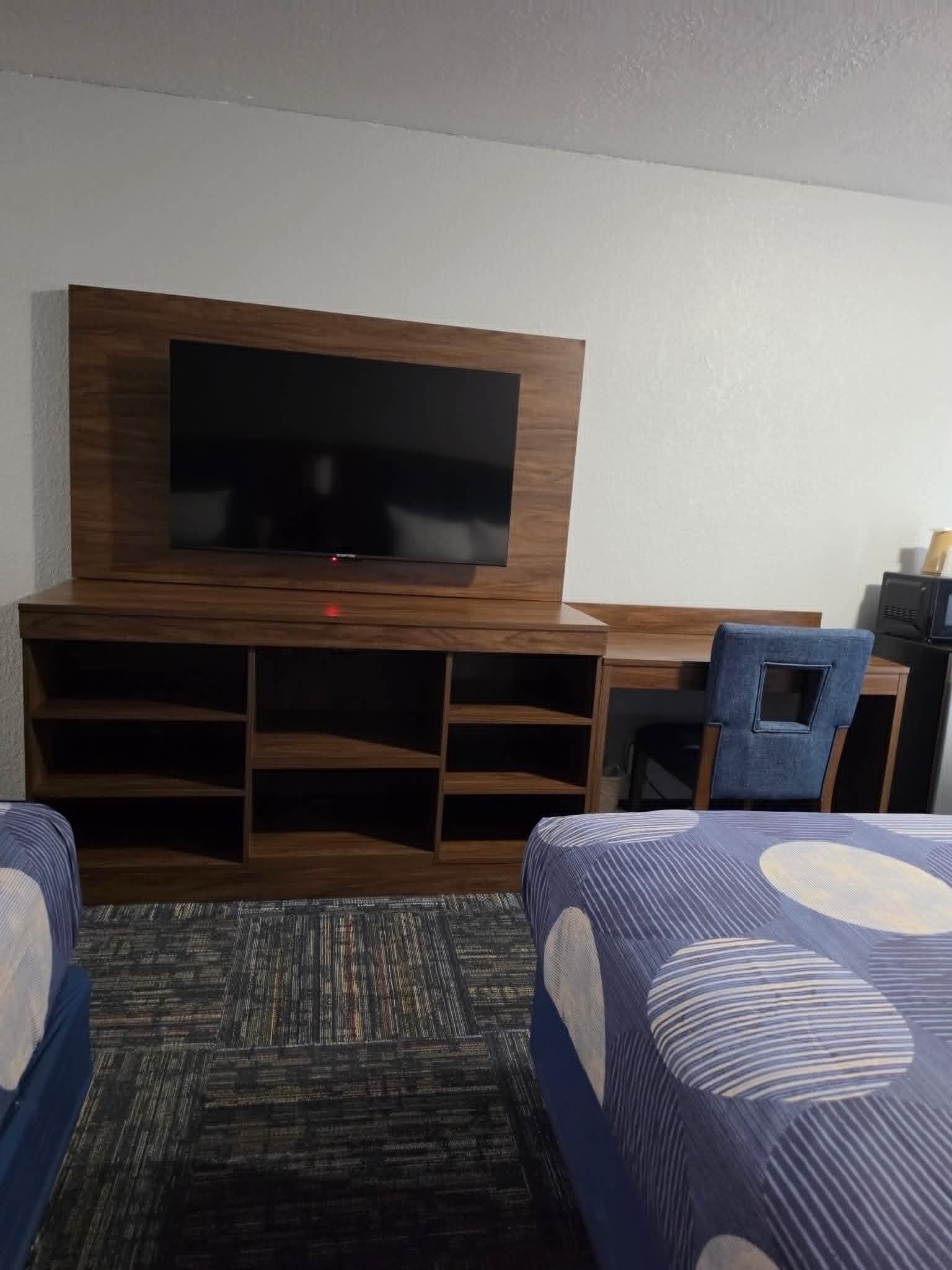 Une chambre d’hôtel équipée d’un téléviseur à écran plat fixé à un meuble en bois, d’un bureau avec une chaise et de deux lits avec une literie à rayures.