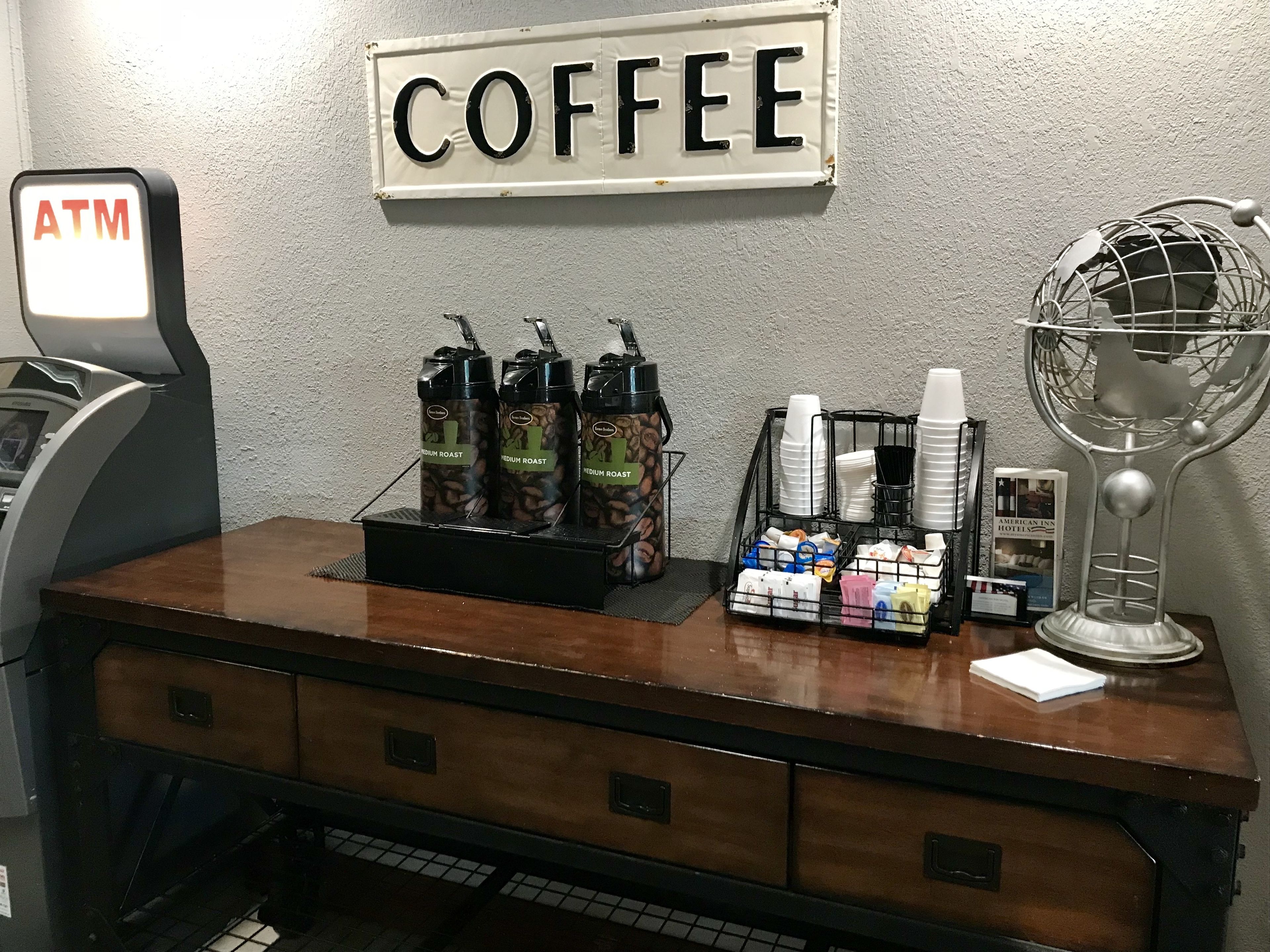A coffee station with an ATM, coffee dispensers, and a globe lamp.