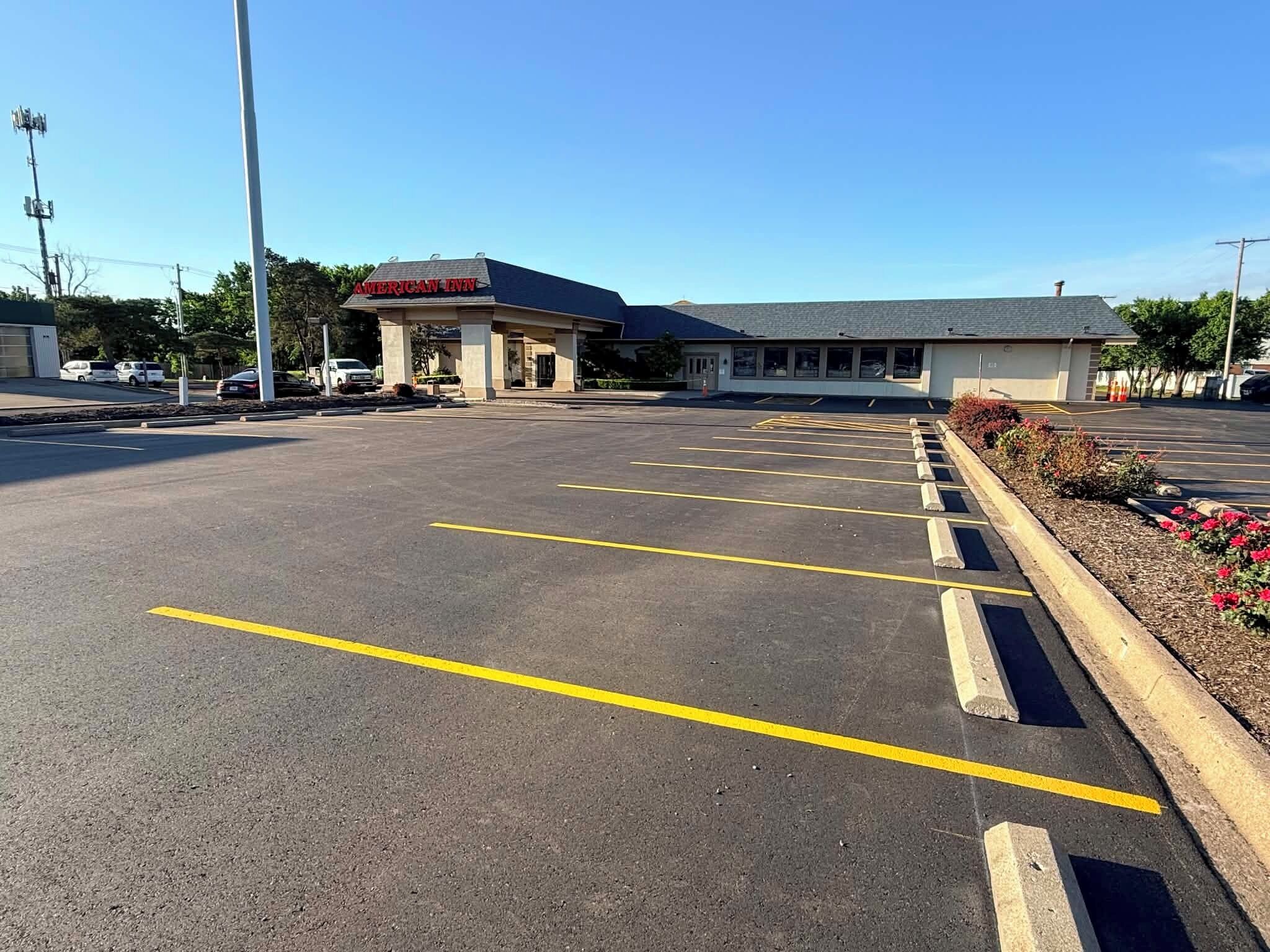 A parking lot with marked spaces, a building labeled 'AMERICAN INN,' and a clear sky.