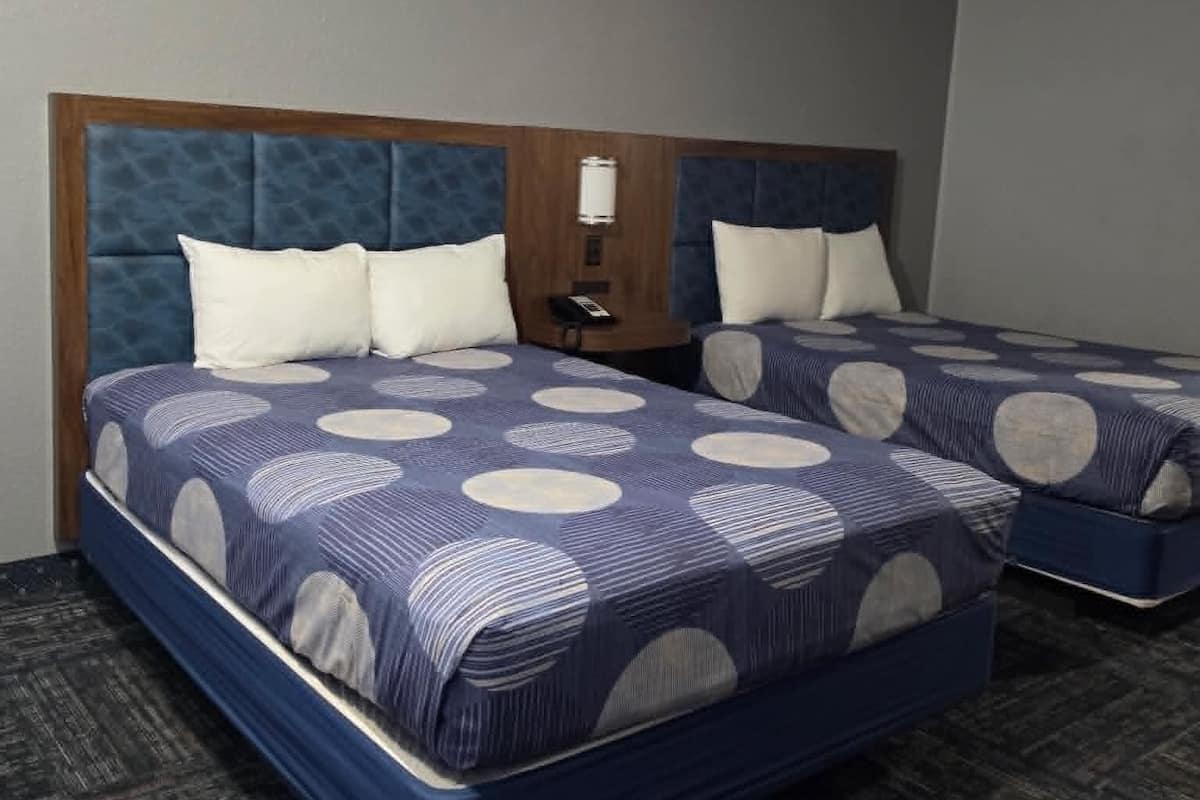 A hotel room with two beds, a wooden headboard, and a carpeted floor.