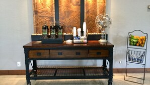 Una zona de bar con mostrador de madera, botellas, un ventilador y una cesta de frutas.
