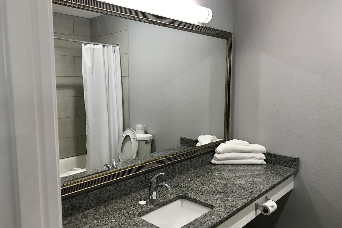 A bathroom with a granite countertop, a white sink, a mirror, a towel rack, and a shower curtain.