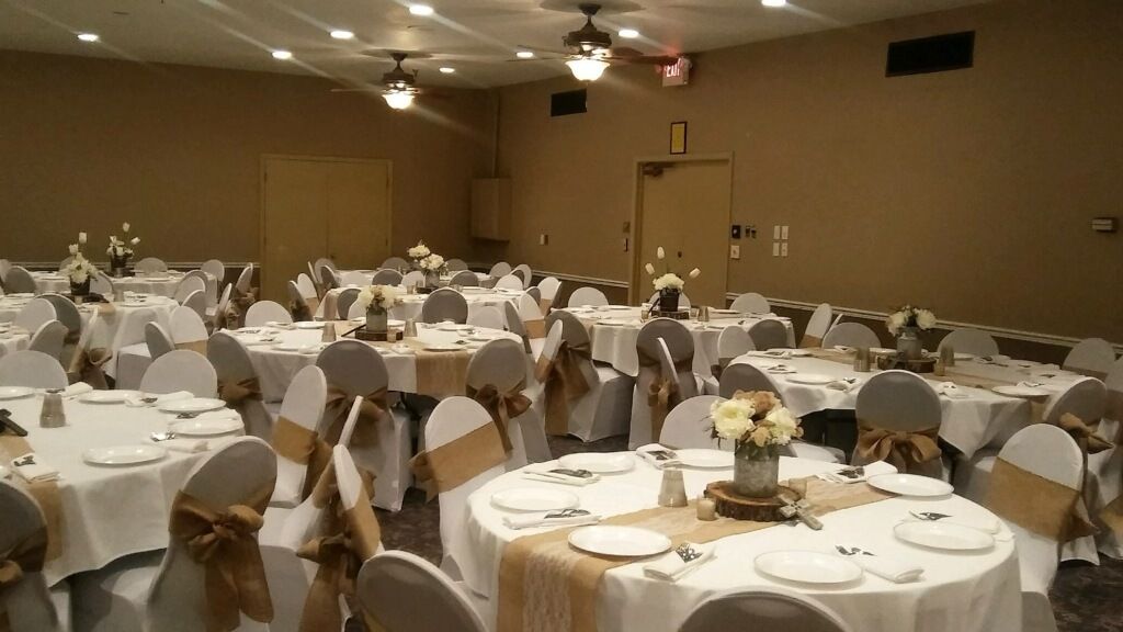 Une salle de banquet avec des tables rondes dressées pour le repas, chacune recouverte d’une nappe blanche et ornée d’un ruban doré.
