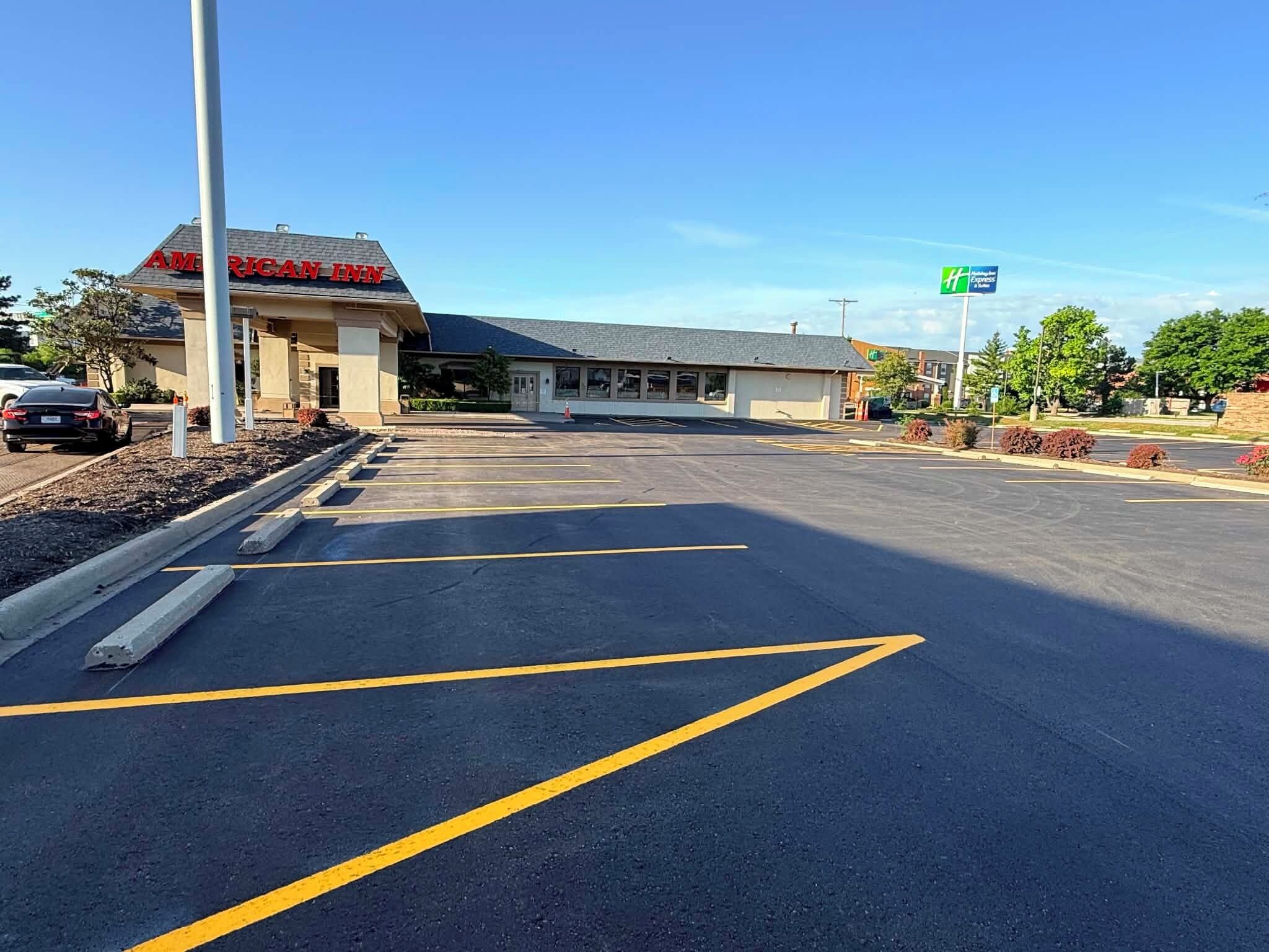 A parking lot with marked spaces, a building with a sign reading 'AMERICAN INN,' and a green sign indicating an expressway.