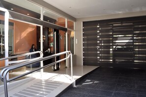A modern hotel lobby with a glass partition, a metal railing, and a large sliding door.