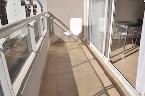 Un balcón con una silla blanca, una mesa de comedor con sillas y vistas a edificios al fondo.