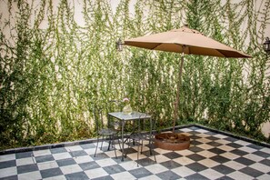 A checkered outdoor patio with a table and chairs, an umbrella, and a decorative planter. - Hotel Gertrudis (Morelia)