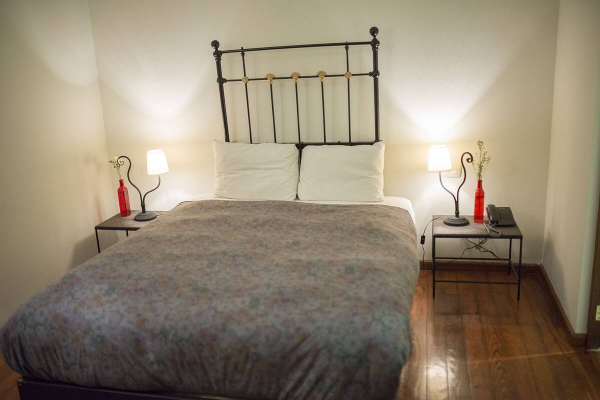 A neatly made bed with a floral bedspread, two bedside tables with lamps, and a wall-mounted light fixture.