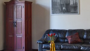 Una sala de estar con un sofá de cuero oscuro, un aparador de madera, una araña y una fotografía en blanco y negro enmarcada en la pared.