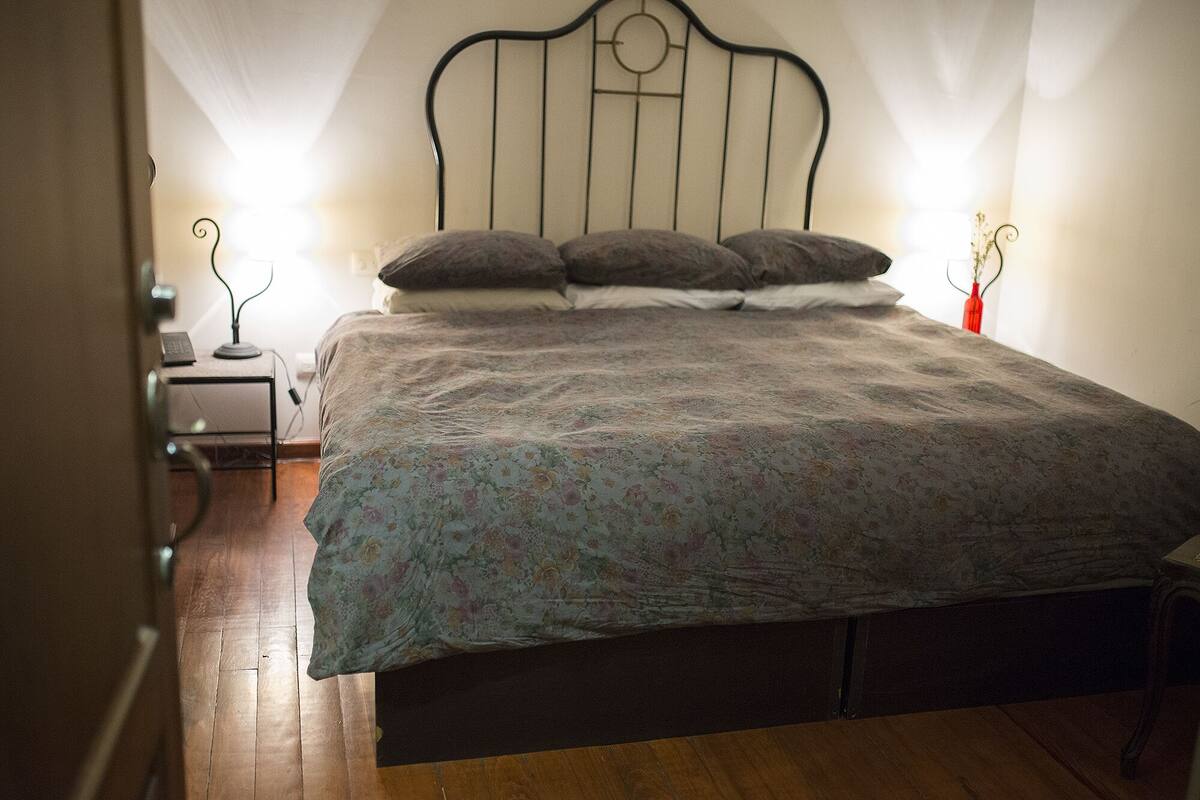 A bedroom with a bed, a nightstand, a lamp, and a red vase on the nightstand.