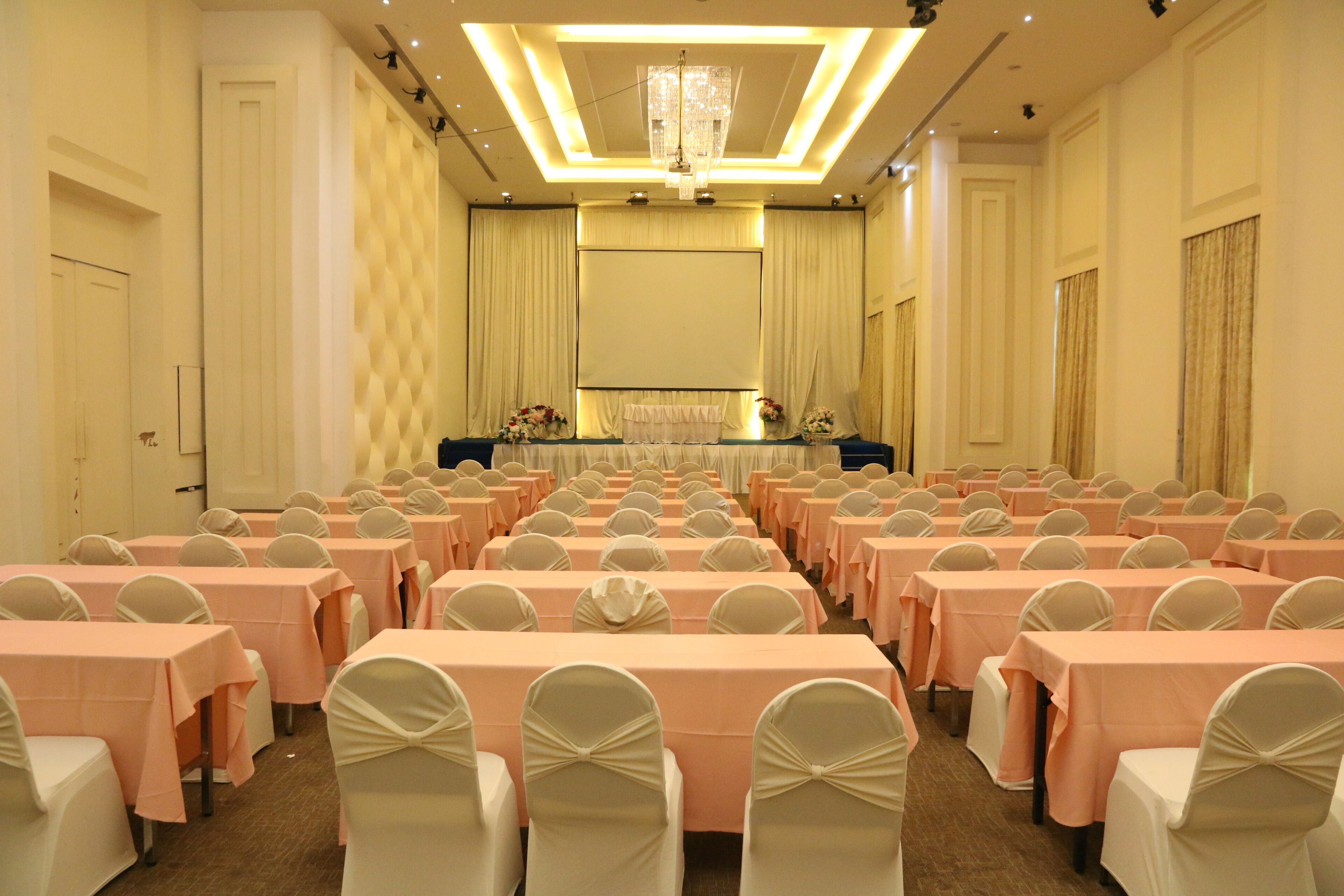 A conference room with rows of tables and chairs, a stage with a podium, and a chandelier.