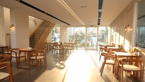 A spacious indoor area with wooden tables and chairs, a staircase, and large windows allowing natural light. - Crystal Palace Luxury Hotel (Pattaya)