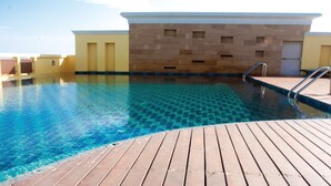 A clear blue pool with a wooden deck, surrounded by beige walls with small windows. - Crystal Palace Luxury Hotel (Pattaya)
