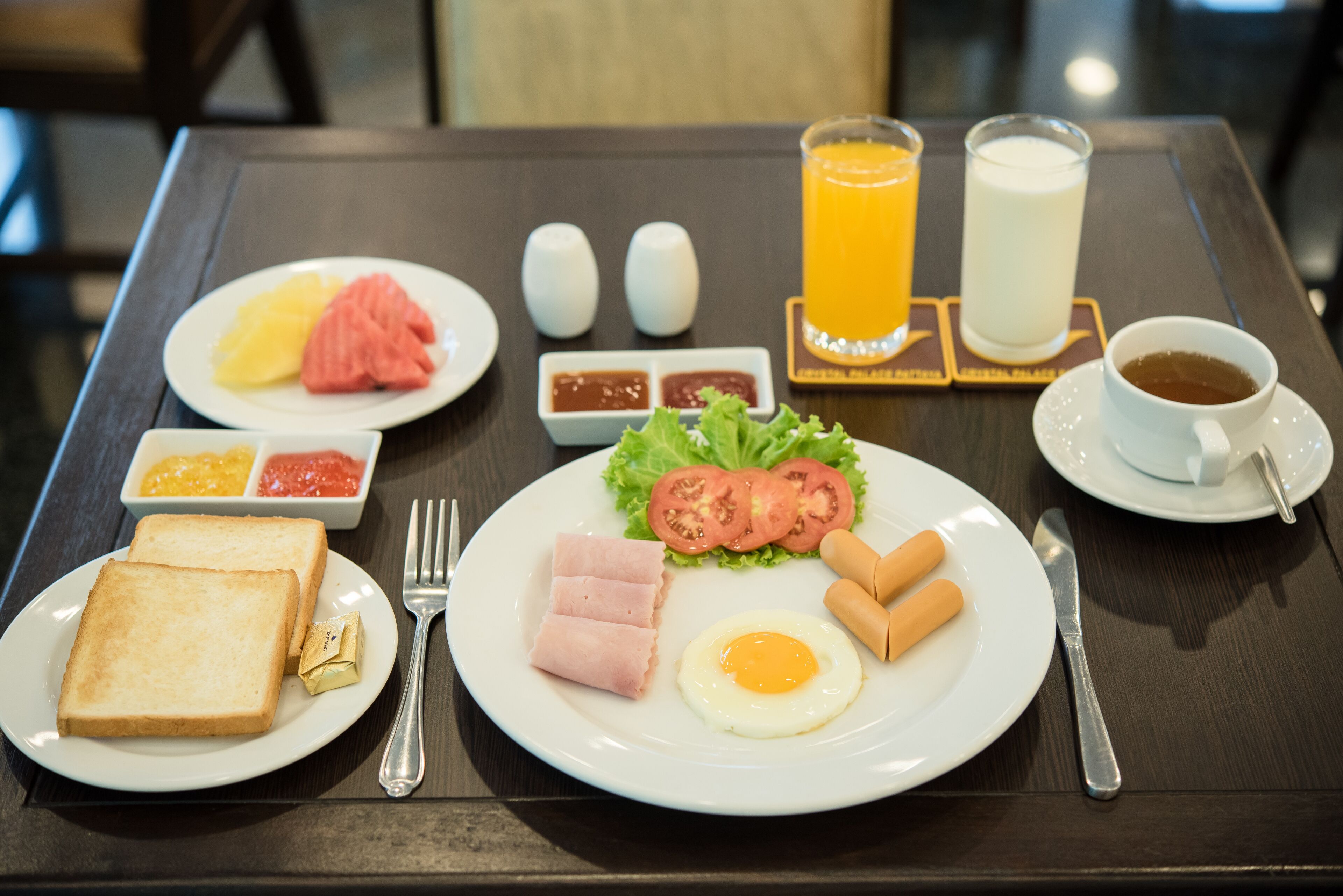 A breakfast setting with toast, ham, eggs, and vegetables on a plate, accompanied by a cup of coffee and a glass of orange juice.