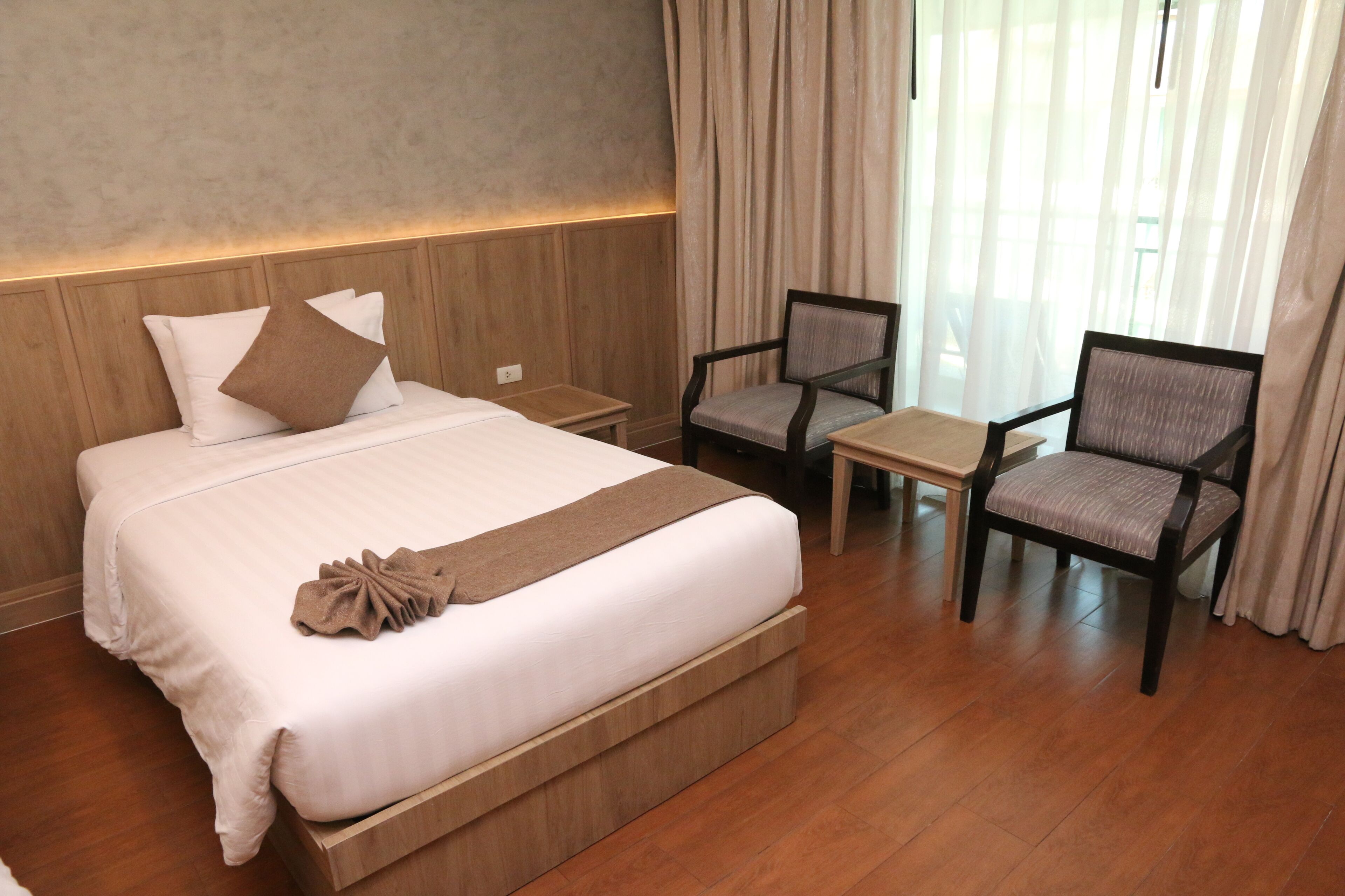 A hotel room with a large bed, two armchairs, a small table, and a nightstand.