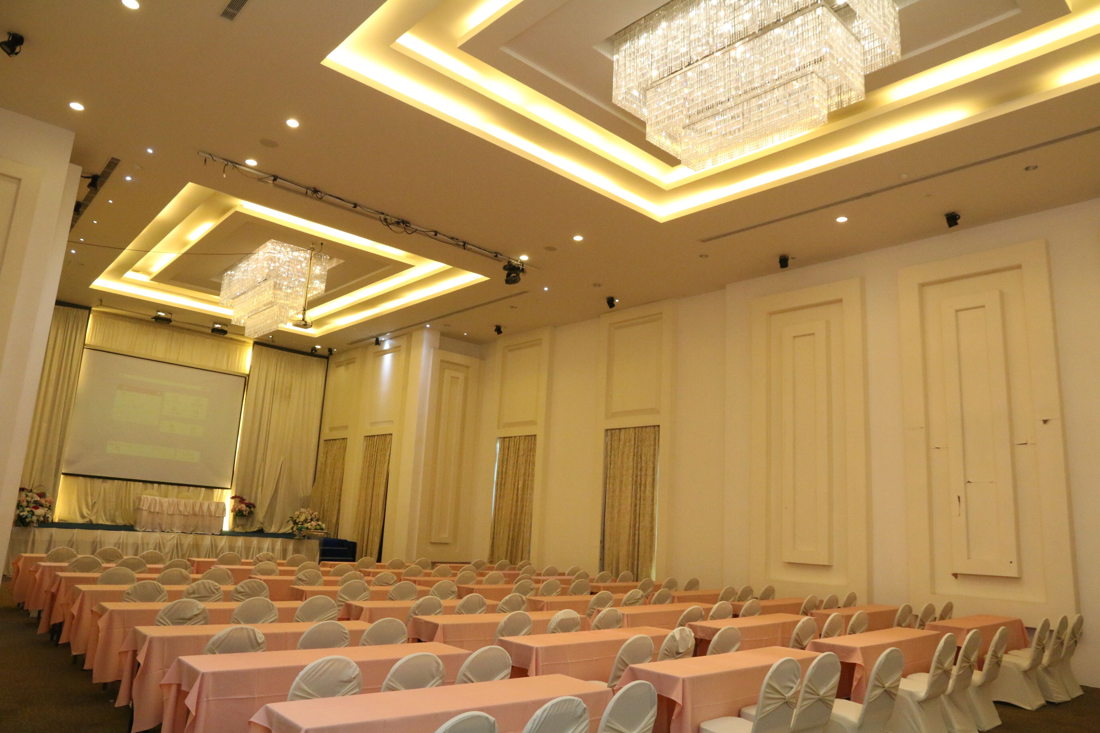 A conference room with rows of tables and chairs, a projector screen, and a chandelier.