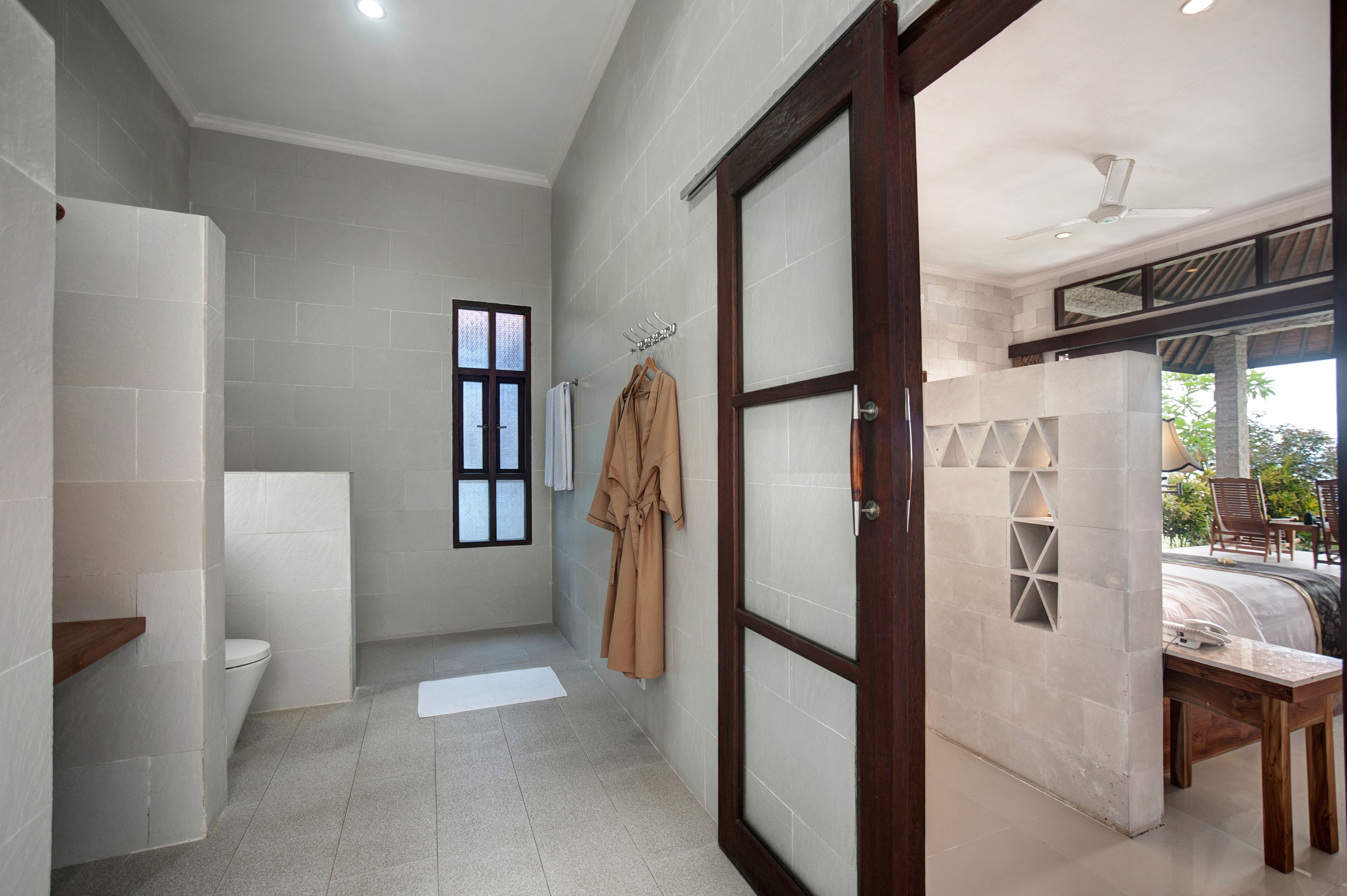 A bathroom with a toilet, a towel rack, and a robe hanging on the wall.